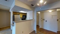 This single-floor unit is designed with a practical, open layout that maximizes functionality. The kitchen is partially enclosed, featuring a pass-through counter with a granite-style surface that connects it to the main living area, creating an accessible and interactive space. The kitchen is equipped with essential appliances, including a stainless steel refrigerator and a built-in microwave, complemented by warm-toned wooden cabinetry and a skylight that introduces natural light overhead.

Adjacent to the kitchen, the living area is fitted with a ceiling fan with integrated lighting, providing both comfort and illumination. The textured popcorn ceiling adds a classic touch throughout the space, while the flooring transitions between carpet and hardwood-style planks, defining different areas of the unit.

A mirrored sliding door opens to a walk-in closet, offering generous storage space with a built-in shelving and hanging rod system, illuminated by an overhead light. The closet's mirrored doors also serve to reflect light and enhance the sense of openness in the surrounding area. Overall, the space presents a functional and straightforward design suited for everyday living.