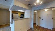 This single-floor unit is designed with a practical, open layout that maximizes functionality. The kitchen is partially enclosed, featuring a pass-through counter with a granite-style surface that connects it to the main living area, creating an accessible and interactive space. The kitchen is equipped with essential appliances, including a stainless steel refrigerator and a built-in microwave, complemented by warm-toned wooden cabinetry and a skylight that introduces natural light overhead.

Adjacent to the kitchen, the living area is fitted with a ceiling fan with integrated lighting, providing both comfort and illumination. The textured popcorn ceiling adds a classic touch throughout the space, while the flooring transitions between carpet and hardwood-style planks, defining different areas of the unit.

A mirrored sliding door opens to a walk-in closet, offering generous storage space with a built-in shelving and hanging rod system, illuminated by an overhead light. The closet's mirrored doors also serve to reflect light and enhance the sense of openness in the surrounding area. Overall, the space presents a functional and straightforward design suited for everyday living.
