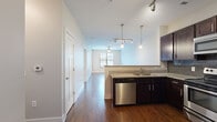 This thoughtfully designed single-floor residence offers an efficient and comfortable layout across its 1 bedroom, 1 bathroom, and dedicated closet. The open-concept kitchen and living area serves as the heart of the home, showcasing rich dark cabinetry, granite countertops, a subway tile backsplash, and a full suite of stainless steel appliances including a range, microwave, dishwasher, and refrigerator. A peninsula with pendant lighting above provides additional counter space and delineates the kitchen from the living area, which benefits from natural light filtering through window blinds and a private entry door with transom window. Durable hardwood-style flooring flows throughout the main living spaces, adding warmth and continuity. The bedroom is a comfortable retreat, featuring soft carpeting, a ceiling fan, and a window with an exterior view, creating a bright and relaxing atmosphere. The full bathroom is finished with large-format floor tiles, a subway-tiled tub-shower combination, a dark-cabinetry vanity topped with granite, and a wide mirror with overhead lighting. A dedicated closet completes the layout, providing practical storage. Track lighting and ceiling fans throughout enhance both functionality and ambiance.