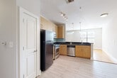 This 1-bedroom, 1-bathroom residence offers a practical and modern layout designed for comfortable everyday living. The open-concept kitchen and living area serves as the heart of the home, where warm hardwood flooring flows seamlessly into the living space. The kitchen is outfitted with light maple cabinetry, dark granite countertops, a soft blue tile backsplash, and a full suite of stainless steel appliances, including a range, microwave, and dishwasher. A peninsula with pendant lighting above and a sink overlooking the living area adds both functionality and style. Track lighting illuminates the kitchen, while natural light filters in through large windows. The living area is open and airy, featuring warm hardwood floors and neutral walls that create a versatile backdrop. A dedicated entryway with a paneled front door and transom window welcomes natural light into the space. The bedroom offers plush gray carpeting, mirrored sliding closet doors, and a calm, neutral palette. The bathroom is finished with tile flooring, a wood vanity with granite countertop, and a subway-tiled tub and shower combination, rounding out this well-designed residence.