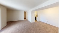 This single-floor unit at Village Square is designed with a practical, straightforward layout that maximizes usable living space. The living area is generously sized, featuring neutral-toned wall-to-wall carpeting and a large sliding glass door dressed with vertical blinds, allowing substantial natural light to fill the room while providing access to the outdoors. A textured ceiling runs throughout the carpeted areas, contributing to the overall character of the space.

Adjacent to the living area, the galley-style kitchen is efficiently arranged with white cabinetry lining both walls, offering ample storage. Light-toned laminate countertops provide workspace alongside a coil-burner electric range and a dishwasher. The kitchen transitions seamlessly into the rest of the unit via an open passageway.

The bedroom is a well-proportioned, quiet space with the same neutral carpet and a window fitted with horizontal blinds, admitting natural light while maintaining privacy.

The full bathroom includes a tiled tub and shower surround in soft yellow tones, a white vanity with an integrated sink, a large wall mirror with overhead lighting, and tile flooring, rounding out this clean and functional unit.