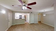 This single-floor residence offers a thoughtfully designed layout that balances comfort and functionality. The open-concept living and dining areas are finished with warm wood-look flooring, neutral gray walls, and textured ceilings, creating a bright and welcoming atmosphere. Ceiling fans are present throughout the main living spaces, providing both style and practicality. Large windows and sliding glass doors flood the interior with natural light while offering views of the surrounding greenery.

The kitchen is a standout feature, boasting white shaker-style cabinetry, a classic tile backsplash, and a full suite of stainless steel appliances including a range, microwave, and refrigerator. A peninsula with a light stone countertop and an integrated sink serves as both a functional workspace and a casual dining area, seamlessly connecting the kitchen to the living space.

The bedrooms are carpeted for comfort and include ceiling fans, louvered closet doors offering ample storage, and access to natural light. The primary bedroom connects directly to a well-lit bathroom featuring a wide double-sink vanity with a light stone countertop, white cabinetry, and a large mirror with an illuminated fixture above. The overall design is clean and move-in ready, with a neutral palette that suits a variety of furnishing styles.