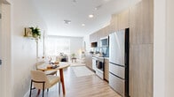 This thoughtfully designed one-bedroom, one-bathroom residence at 50 Salt Street in Revere, Massachusetts offers a contemporary open-concept layout that maximizes every square foot. Light wood-tone flooring flows throughout, complementing the bright white walls and recessed lighting that give the space a clean, modern feel.

The kitchen is a standout feature, outfitted with flat-front cabinetry in a warm wood finish, a striking navy blue tile backsplash, stainless steel appliances including a range, built-in microwave, dishwasher, and a full-size refrigerator, and white quartz countertops. The kitchen opens seamlessly to a dining area and living space, making the layout ideal for everyday living and entertaining.

The living area is bright and inviting, with a large window that draws in natural light and creates an airy atmosphere. The generously sized bedroom continues this bright aesthetic, featuring another large window, light hardwood flooring, and ample room for a full furniture arrangement. A dedicated closet provides practical storage.

The bathroom is finished with marble-look tile flooring and a walk-in glass-enclosed shower with full-height tile surround and chrome fixtures, offering a sleek, spa-like feel. The overall design of this Revere unit balances modern aesthetics with functional, everyday comfort.