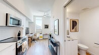 Located at 4225 SE Milwaukie Ave in Portland's vibrant SE neighborhood, this efficiently designed studio offers a thoughtful layout that maximizes every square foot. The single-floor plan integrates a living room, kitchen, and bathroom in a cohesive, modern aesthetic defined by crisp white walls and warm light wood flooring throughout.

The living area is a bright, welcoming space anchored by tall windows that flood the room with natural light and offer views of the surrounding neighborhood. A functional workspace with a wooden desk complements the relaxed seating area, making the space well-suited for both work and leisure.

The galley-style kitchen is sleek and well-appointed, featuring white cabinetry, stainless steel appliances including a refrigerator, electric range, and microwave, as well as a single-basin sink. Recessed lighting and clean lines give the kitchen a polished, contemporary feel.

The bathroom continues the minimalist design language with light wood flooring, white walls, matte black hardware accents, and a shower with a curtain enclosure. The space is clean, functional, and uncluttered.

Throughout, the studio maintains a consistent modern sensibility — neutral tones, quality finishes, and an open, airy atmosphere that makes this compact Portland residence feel both practical and inviting.