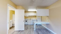This single-floor unit offers a practical and well-organized layout designed for comfortable everyday living. The kitchen is a central feature of the space, outfitted with white cabinetry, a electric range, dishwasher, full-size refrigerator, and a stainless steel sink — all set against warm yellow walls and light wood-style flooring that extends throughout the main living areas. A white dining table is positioned adjacent to the kitchen, creating a convenient and connected dining area.

The open living and kitchen area flows seamlessly, offering a bright and airy atmosphere enhanced by flush-mounted lighting and a ceiling fan. The space also includes a wall-mounted air conditioning unit for year-round climate control.

The bedroom is carpeted for added warmth and comfort, featuring a window with blinds that allows natural light to filter in. A ceiling fan and wall-mounted A/C unit are also present, ensuring a comfortable environment. The room's neutral beige tones contribute to a calm and restful atmosphere.

The bathroom is clean and functional, featuring a full-size soaking tub with a tiled shower surround, a toilet, and a vanity with countertop space. The wood-style flooring continues here, tying the space together with a cohesive aesthetic throughout.
