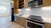 Located at 3000 W Clay St in Richmond, Virginia, this single-floor unit offers a thoughtfully designed, modern living space. The open-concept living and kitchen area is anchored by warm wood-tone cabinetry that extends floor to ceiling, providing generous storage alongside open shelving. The kitchen is equipped with a full suite of stainless steel appliances, including a refrigerator, electric range, over-the-range microwave, and dishwasher, complemented by clean white quartz countertops and a classic subway tile backsplash with under-cabinet lighting. Durable wood-look plank flooring runs throughout the main living area, enhancing the contemporary aesthetic. A large window in the living area brings in natural light and offers views of the surrounding neighborhood. The bedroom is carpeted for comfort and features a generous picture window with sweeping city views, creating a bright and airy retreat. The bathroom is finished with neutral tile flooring, a wood-front vanity with a white countertop, and a full tub-shower combination adorned with clean white subway tile and a curved chrome rod. Recessed lighting throughout the unit adds to the polished, move-in-ready feel of this well-appointed Richmond residence.