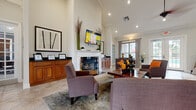 Located at 105 Brookhaven Ct N in Palm Coast, Florida, this single-floor space offers a thoughtfully designed layout encompassing a living room, dining area, kitchen, and a dedicated office. The living room is a standout feature, boasting soaring vaulted ceilings with crown molding, recessed lighting, and a ceiling fan. A classic white fireplace serves as the room's focal point, flanked by warm wood cabinetry and complemented by large-format tile flooring. French doors and expansive windows allow abundant natural light to flow throughout, creating a bright and welcoming ambiance. The open-concept design connects the living area seamlessly to the dining space, which features a round glass-top dining table and direct views to the outdoors. A pass-through counter with decorative wood corbels links the main area to the kitchen, which is equipped with rich wood cabinetry, dark granite countertops, and a tile backsplash. The dedicated office is carpeted and well-lit by multiple windows, offering a quiet and functional workspace. The entry foyer makes a strong first impression with its high ceiling, tile flooring, and elegant French doors leading further into the space. Overall, the design balances practicality with refined detail throughout.