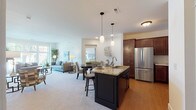 This well-appointed single-floor residence is designed with an open-concept layout that seamlessly connects the kitchen, dining, and living areas. The kitchen is a standout feature, equipped with rich dark-stained wood cabinetry extending to the ceiling, stainless steel appliances including a French door refrigerator, electric range, and built-in microwave, all complemented by light stone countertops and hardwood flooring. A dark-finished center island with a granite top, undermount sink, and pendant lighting above serves as both a functional workspace and casual seating area.

The living room is bright and inviting, anchored by a tile-surround fireplace with a wood mantle and large windows that bring in generous natural light and outdoor views. Soft carpeting flows throughout the living and bedroom areas.

The primary bedroom is spacious with a large window overlooking greenery, while a secondary bedroom features a mirrored closet and direct access to a bathroom. The full bathroom offers an extended vanity with white cabinetry, stone countertops, and tile flooring. A dedicated laundry room with side-by-side washer and dryer and upper cabinetry adds everyday convenience throughout this thoughtfully designed home.