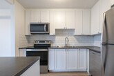 Located at 1189 Talwood Court in Peterborough, Ontario, this one-bedroom, one-bathroom unit offers a thoughtfully designed open-concept layout finished with light hardwood-style flooring throughout. The combined living, dining, and kitchen area forms the heart of the unit, bathed in natural light from large sliding glass doors that open to an outdoor balcony with views of the surrounding neighbourhood. A half-wall peninsula with a dark countertop provides a natural division between the living and kitchen areas while maintaining an open feel. The kitchen is well-appointed with white shaker-style cabinetry, grey stone countertops, a classic white subway tile backsplash, and stainless steel appliances including an electric range, over-the-range microwave, and refrigerator. The bedroom is a comfortable, private space featuring its own large sliding glass door for natural light and outdoor access. Baseboard heating runs along the perimeter of multiple rooms, ensuring efficient warmth throughout. The bathroom is finished with a full-sized soaker tub and shower, surrounded by crisp white subway tile. Clean white walls and a textured ceiling complete the bright, modern aesthetic of this well-maintained unit.