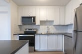 Located at 1189 Talwood Court in Peterborough, Ontario, this one-bedroom, one-bathroom unit offers a thoughtfully designed open-concept layout finished with light hardwood-style flooring throughout. The combined living, dining, and kitchen area forms the heart of the unit, bathed in natural light from large sliding glass doors that open to an outdoor balcony with views of the surrounding neighbourhood. A half-wall peninsula with a dark countertop provides a natural division between the living and kitchen areas while maintaining an open feel. The kitchen is well-appointed with white shaker-style cabinetry, grey stone countertops, a classic white subway tile backsplash, and stainless steel appliances including an electric range, over-the-range microwave, and refrigerator. The bedroom is a comfortable, private space featuring its own large sliding glass door for natural light and outdoor access. Baseboard heating runs along the perimeter of multiple rooms, ensuring efficient warmth throughout. The bathroom is finished with a full-sized soaker tub and shower, surrounded by crisp white subway tile. Clean white walls and a textured ceiling complete the bright, modern aesthetic of this well-maintained unit.