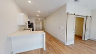 Located at 8000 Arlington Expressway in Jacksonville, FL, this 1-bedroom, 1-bathroom unit offers a clean, modern design across a single floor. Light wood-tone flooring flows throughout the entire space, creating a cohesive and bright aesthetic. The open-concept living area seamlessly connects the kitchen, dining, and living spaces, with large floor-to-ceiling windows at the far end flooding the interior with natural light. The kitchen is well-equipped with white shaker-style cabinetry, stainless steel appliances including a refrigerator, electric range, and built-in microwave, complemented by a double-basin sink and ample countertop space. A peninsula divides the kitchen from the living and dining area, which features recessed lighting and a roller shade on the expansive window. The bedroom is a comfortable, well-lit space with a ceiling fan and direct access to the bathroom. The bathroom includes a white vanity with a single sink, large mirror, and a glass-enclosed walk-in shower. A sliding barn-style door adds a modern touch to the layout. The unit also includes a dedicated closet and in-unit laundry, rounding out a practical and functional living space.