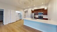 Located on East Market Street in Greensboro, NC, this thoughtfully designed single-floor residence combines modern aesthetics with functional living. The open-concept main living area is anchored by striking floor-to-ceiling windows with bold black framing, flooding the space with natural light and offering views of the surrounding neighborhood. A glass door leads to a private balcony with metal railings, extending the living space outdoors. Light-toned hardwood flooring runs throughout, complementing the clean white walls and recessed lighting overhead.

The kitchen is a standout feature, centered around a generous island with a white quartz countertop, undermount sink, and pendant lighting. Rich walnut-toned cabinetry reaches to the ceiling, paired with a herringbone tile backsplash and a full suite of stainless steel appliances. An in-unit laundry area is conveniently accessible nearby.

The bedrooms are well-proportioned, each featuring large grid-paned windows, ceiling fans, and hardwood floors. The bathrooms are finished with marble-style tile flooring and wall surrounds, warm wood vanities with white countertops, and brushed nickel hardware. The primary bath includes a spacious walk-in closet with built-in shelving. A secondary full bath offers a tub-shower combination with tiled surround.