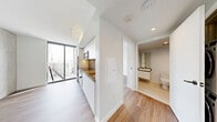Located at 707 Terry Ave in the heart of Seattle, WA, this efficiently designed one-bedroom, one-bathroom unit offers a modern urban living experience across a single floor. Light wood flooring flows throughout, complementing a clean, contemporary aesthetic defined by crisp white walls and minimalist finishes.

The open kitchen is outfitted with flat-front white cabinetry extending to the ceiling, stainless steel appliances including a refrigerator, oven, and microwave, a warm-toned backsplash, and a sleek countertop with an undermount sink. Floor-to-ceiling windows flood the kitchen and adjacent living area with natural light while framing sweeping elevated views of the Seattle skyline and surrounding cityscape.

The bedroom is a serene, light-filled space featuring its own floor-to-ceiling sliding glass door that opens to city views, providing an airy feel. The clean white walls and warm wood flooring keep the room simple and inviting.

A hallway connects the main living areas to the bathroom, which features a full soaking tub set against dramatic dark stacked tile walls, a wall-mounted sink, and polished chrome fixtures — a striking contrast to the otherwise light and airy palette of the unit. The overall design is cohesive, contemporary, and thoughtfully composed for efficient urban living.