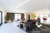 Located at 3915 Degree Lane in Mountain View, California, this single-floor amenity lounge is thoughtfully designed to encourage both socializing and relaxation. The interior showcases a contemporary aesthetic defined by light wood wall paneling, smooth large-format tile flooring, and recessed lighting that creates a bright, welcoming atmosphere throughout.

The main lounge area is anchored by a modular sectional sofa with colorful accent pillows, complemented by a sleek, dark-surfaced central table and additional ottomans for flexible seating arrangements. A standout design feature is the accent wall adorned with horizontal moss panels, adding a vibrant, living element to the otherwise neutral palette. Suspended egg-shaped hanging chairs provide a playful and informal seating option nearby.

An adjacent zone offers a dedicated workspace or casual dining area with a built-in desk, modern chairs, and a bold geometric-patterned accent wall. A foosball table adds a recreational dimension to the space.

Large floor-to-ceiling sliding glass doors open seamlessly onto a generously sized outdoor terrace finished with a checkered tile pattern. The terrace includes string lighting overhead, raised planters, and a ping pong table, offering open-air views of the surrounding Mountain View neighborhood and distant hills.
