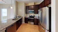 Located on the third floor at 3220 Centennial Way in Frederick, MD, this apartment offers a thoughtfully designed single-level layout with a clean, neutral aesthetic throughout. The open-concept living area serves as the heart of the unit, featuring light hardwood-style flooring, warm beige walls, and a classic white-surround fireplace that anchors the main living space. The layout flows naturally between the living area and kitchen, making the space feel connected and functional.

The kitchen is well-appointed with rich, dark espresso-toned cabinetry offering generous storage, granite countertops with speckled detailing, and a curved peninsula with an undermount sink—ideal for casual dining or meal prep. Stainless steel appliances, including a refrigerator, range, and over-the-range microwave, complete the kitchen. Pendant lighting and a track light fixture add focused illumination throughout the space.

The bedroom is carpeted for comfort and features a large window with blinds, allowing natural light and exterior views of the surrounding community. The bathroom includes tile flooring, a full soaking tub with a subway-tiled surround, and chrome fixtures, providing a clean and functional design. Overall, the unit presents a practical and comfortable living environment with modern finishes.