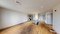 Located at 1 East Main in Bay Shore, NY, this thoughtfully designed one-bedroom, one-bathroom unit offers a clean, modern aesthetic throughout its efficiently utilized single floor. The open-concept layout seamlessly connects the living area to the kitchen, creating a bright and cohesive living space. Recessed lighting and crisp white walls enhance the airy feel throughout.

The kitchen is a standout feature, equipped with stainless steel appliances including an electric range, built-in microwave, and refrigerator. Warm-toned wood cabinetry pairs with light quartz countertops, and a peninsula island with a stainless steel sink adds both functionality and style. Wood-look plank flooring runs consistently throughout the main living areas, adding warmth and continuity.

The bedroom is a comfortable, well-proportioned room with natural light provided by dual windows fitted with blinds, wood-look flooring, and a dedicated closet for storage. The bathroom features a full soaking tub and shower combination, framed by floor-to-ceiling rectangular tile in a neutral taupe tone, complemented by clean white fixtures and chrome hardware.

The living room offers ample wall space and natural light from multiple windows, making it a versatile and welcoming area. The unit also includes a dedicated closet and modern panel-style interior doors throughout.
