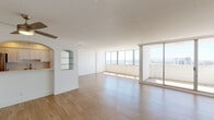 This well-appointed high-rise residence is designed with a clean, modern aesthetic throughout. The centerpiece of the home is a generously sized open living area, bathed in abundant natural light streaming through a dramatic wall of floor-to-ceiling windows. These windows frame sweeping panoramic views of the surrounding cityscape, creating a bright and airy atmosphere. Light wood-tone flooring extends throughout the main living spaces, complementing the crisp white walls and textured ceilings. A stylish arched niche with glass shelving serves as a charming architectural accent, while a partial partition wall divides the living area from the kitchen. The galley-style kitchen is thoughtfully designed with contrasting dark lower cabinetry and white upper cabinets, white quartz countertops, stainless steel appliances including a refrigerator and dishwasher, and a deep undermount sink. A sliding glass door leads to a private balcony, extending the living space outdoors. The bedroom features plush carpeting and a closet, offering a comfortable retreat. Both bathrooms are finished with wood-look flooring, dark cabinetry with chrome hardware, white quartz vanity tops, large mirrors, and tiled shower enclosures. The overall ambiance is light, clean, and contemporary.