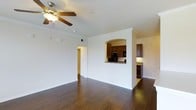 This single-floor, one-bedroom, one-bathroom residence offers a well-organized layout that maximizes everyday comfort. The living area is a welcoming, open space highlighted by rich dark hardwood flooring that extends throughout, creating a warm and cohesive aesthetic. Crown molding lines the upper edges of the walls, adding a refined architectural detail, while a ceiling fan with a light fixture provides both practical airflow and ambient lighting.

A distinctive arched pass-through opening connects the living area to the kitchen, offering an open feel while maintaining a defined separation between spaces. The kitchen features rich, dark wood cabinetry paired with granite-style countertops and black appliances, including a full-size refrigerator. The cabinetry provides generous storage, and the layout allows for efficient use of the space.

White walls throughout keep the interior feeling bright and airy, complementing the contrast of the dark flooring and cabinetry. A hallway visible from the main living area leads to the remaining rooms, maintaining a logical and functional flow. The overall ambiance is clean, comfortable, and move-in ready, offering a balanced blend of practical design and tasteful finishes.