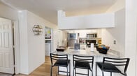 This single-floor residence offers a functional and modern layout across three bedrooms and three full bathrooms. The open-concept kitchen and living area serves as the heart of the home, featuring a granite-topped breakfast bar with seating, stainless steel appliances including a refrigerator, microwave, and range, and white cabinetry providing ample storage. Light wood-style flooring runs throughout, contributing to a clean, cohesive aesthetic. The galley-style kitchen offers well-organized counter space and generous cabinet storage along both walls.

The living area provides a comfortable gathering space with neutral tones and natural light. Each bedroom is thoughtfully sized, featuring ceiling fans, wood-style flooring, closet storage, and windows with curtains. The primary bedroom offers a comfortable footprint with room for a full workspace and storage. The three full bathrooms are finished consistently with granite-topped vanities, white cabinetry, tub-shower combinations, and wood-style flooring. A hallway connects the bedrooms and provides access throughout the unit. Notably, an in-unit washer and dryer is conveniently accessible near the main living area, adding a practical amenity to this well-designed residence.