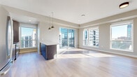 This single-floor urban residence showcases a thoughtfully designed open-concept layout with clean, contemporary finishes throughout. The main living area is anchored by light hardwood flooring and features large floor-to-ceiling windows and a sliding glass door leading to a private balcony, offering sweeping city views and filling the space with generous natural light.

The kitchen is well-appointed with two-tone cabinetry — combining white upper cabinets with dark wood lower cabinets — a subway tile backsplash, quartz countertops, a central island with pendant lighting, and a full suite of stainless steel appliances. The open flow between the kitchen and living area creates an ideal layout for both daily living and entertaining.

The bedrooms are carpeted for comfort and each feature large windows with city views and sliding closets with built-in shelving. The bathrooms are finished with floating dark wood vanities, white quartz countertops, undermount sinks, and framed mirrors. The primary bathroom offers a dual-sink vanity and ample storage cabinetry. A dedicated laundry closet houses a stacked full-size washer and dryer for added convenience. The overall palette of warm neutrals and modern materials creates a cohesive, polished ambiance throughout.