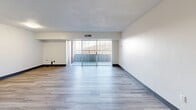 Located at 1100 Penn Center Blvd in Pittsburgh, PA, this single-floor unit offers a straightforward and functional layout designed for comfortable everyday living. The living area is bright and open, featuring light-toned vinyl plank flooring and clean white walls accented by bold dark baseboards. A sliding glass door floods the space with natural light and provides direct access to a private balcony, offering outdoor views of the surrounding area. The textured ceiling and built-in ventilation contribute to the room's practical design.

The kitchen is efficiently laid out with white cabinetry, granite-style countertops, and white appliances including a refrigerator and electric range. Light wood-toned vinyl flooring continues throughout this area, maintaining a cohesive aesthetic. A secondary room, also finished with vinyl plank flooring in a complementary gray tone, offers versatile use and includes a built-in shelf detail along one wall.

The bathroom is finished with full white ceramic tile surrounding a soaking tub and shower combination, complemented by chrome fixtures and a clean, minimalist design. Throughout the unit, the neutral color palette, updated flooring, and consistent finishes create a tidy, move-in-ready environment well-suited for practical, low-maintenance living.