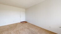 Located at 5025 N 1st Ave in Tucson, Arizona, this one-bedroom, one-bathroom unit offers a practical and well-organized layout across a single floor. The spacious living room serves as the heart of the home, featuring neutral-toned wall-to-wall carpeting, crisp white walls, and a textured ceiling. A large window allows generous natural light to flow in, offering pleasant outdoor views and creating a bright, open atmosphere. The front entry opens directly into this comfortable living area, providing a welcoming first impression. The galley-style kitchen is efficiently designed with warm wood cabinetry, white appliances including an electric range, refrigerator, and dishwasher, complemented by a window that brings in additional natural light. Hardwood-style flooring grounds the kitchen space and carries into the bathroom. The bedroom is a well-proportioned retreat with soft carpeting, a window with louver shutters for light control, and direct access to a dedicated closet. The bathroom features a wide vanity with wood cabinetry, a large mirror, a well-lit vanity fixture, and hardwood-style flooring, providing a clean and functional space. Throughout the unit, the consistent use of neutral tones and natural materials creates a cohesive and comfortable living environment.