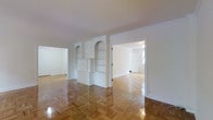 This single-floor space showcases a thoughtfully designed interior that blends classic architectural details with a clean, open layout. The most striking feature underfoot is the beautifully polished herringbone parquet hardwood flooring, which adds warmth and timeless character throughout the space. Crisp white walls and bright ceilings create a light-filled atmosphere that enhances the sense of openness across the interconnected rooms.

A central built-in shelving unit serves as a functional and decorative focal point, featuring a combination of open shelving, lower cabinet storage, and a charming arched display niche. This built-in seamlessly divides areas of the space while maintaining visual connectivity. Crown molding along the ceiling adds a refined architectural touch that complements the overall classic aesthetic.

The layout flows naturally from one room to the next, with wide doorways allowing an easy transition between spaces. Adjacent rooms are equally bright, benefiting from generous natural light and the same consistent flooring and neutral color palette. The overall ambiance is clean, airy, and versatile, offering a welcoming and adaptable environment well-suited for a variety of uses.