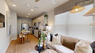 This two-story, 1-bedroom, 2-bathroom residence is thoughtfully designed to maximize every square foot across both levels. The main floor hosts an open-plan kitchen and living area, where light wood-look flooring flows seamlessly throughout. The kitchen is outfitted with crisp shaker-style cabinetry in a soft gray-white tone, granite countertops, a white subway tile backsplash, and a full suite of stainless steel appliances including a French door refrigerator, range with over-the-range microwave, and dishwasher. A marble-top dining table provides casual dining space adjacent to the kitchen. The living area is bright and welcoming, featuring large windows with horizontal blinds that invite abundant natural light and outdoor views. A powder room with granite vanity and wood-look flooring completes the main level. Upstairs, the primary bedroom is a serene retreat with plush carpeting, a ceiling fan, and generous corner windows dressed in sheer curtains that frame lush outdoor views. A dedicated closet and full bathroom — featuring a soaking tub with marble-style tile surround and granite vanity — accompany the bedroom. The hallway connects all upper-level spaces with ease, rounding out a clean, functional, and modern layout.