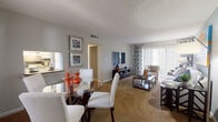 This single-story residence is thoughtfully laid out to maximize comfort and functionality across its living spaces. The open-concept living and dining area serves as the heart of the home, featuring plush carpeting, a textured ceiling, and large sliding glass doors dressed with patterned drapes that allow generous natural light to fill the space. The living room comfortably accommodates a full seating arrangement alongside a media console, while the adjacent dining area provides space for a glass-top table and upholstered chairs.

The kitchen is finished with warm wood-style flooring, white cabinetry, a drop ceiling with recessed lighting, and a window above the sink. It includes a full suite of appliances—refrigerator, range, dishwasher—and ample counter space. A hallway with additional cabinetry and louvered closet doors connects the main living spaces to the private quarters.

Both bedrooms are carpeted and well-sized. The primary bedroom features a bold accent wall, a walk-in closet with built-in shelving, and a window with natural light. The secondary bedroom offers a quiet, neutral palette with a dresser area and closet access. The bathroom includes a tiled tub-shower combination with classic white finishes, completing this well-appointed home.