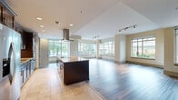 Located at 2121 North Westmoreland Street in Arlington, VA, this 2-bedroom, 3-bathroom single-floor residence offers a thoughtfully designed open-concept layout with generous living space. The combined kitchen and living area serves as the heart of the home, featuring large floor-to-ceiling windows on multiple walls that flood the space with natural light and provide views of lush greenery outside. The kitchen is appointed with rich dark-wood cabinetry, granite countertops, a central island with a built-in cooktop, a stainless steel hood vent, double wall ovens, and a full suite of stainless steel appliances. Tile flooring transitions seamlessly into wide-plank hardwood that extends throughout the living areas and bedrooms. The primary bedroom is a spacious retreat with a ceiling fan and direct access to a well-appointed en-suite bathroom featuring a glass-enclosed shower, a soaking tub with a window view, tile flooring, and dark-wood vanity cabinetry. The second bedroom offers a clean, neutral palette with hardwood floors. Two walk-in closets with wire shelving provide ample storage. A dedicated laundry room houses a full-size washer and dryer. The layout is completed by three hallways and three full bathrooms, ensuring comfort and functionality throughout.