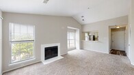 Located at 1623 Parkridge Cir in Crofton, Maryland, this single-floor residence offers a well-designed layout with notable architectural character throughout. The living area is a standout feature, boasting soaring vaulted ceilings that create an airy, open atmosphere. A classic white-surround fireplace serves as the focal point of the room, complemented by plush wall-to-wall carpeting and multiple windows that draw in abundant natural light. The open pass-through to the kitchen maintains a connected feel between living and dining areas. The kitchen is equipped with stainless steel appliances, including a refrigerator, range, and over-the-range microwave, set against a crisp white subway tile backsplash and light-toned cabinetry with modern hardware. Wood-look flooring adds a warm, durable finish to the kitchen space. The primary bedroom is generously proportioned with vaulted ceilings, a louvered closet, an en-suite area, and sliding glass doors opening to a private balcony overlooking lush greenery. An additional bedroom features a large window framing views of mature trees, and is finished with soft carpeting. The bathroom includes a full tub-shower combination with tile surround, a single vanity with ample counter space, and wood-look flooring that ties the space together cohesively.