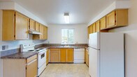 This single-floor residence features 2 bedrooms and 2 bathrooms within a practical and thoughtfully arranged floor plan. The U-shaped kitchen is outfitted with warm honey-toned wood cabinetry, dark laminate countertops, white appliances including a range, dishwasher, and refrigerator, and durable tile-style flooring. A window above the sink allows natural light to brighten the space. The adjoining living room is carpeted and features a sliding glass door that opens to an outdoor patio area, providing both natural light and exterior access. The primary bedroom offers a comfortable amount of space, complemented by a built-in closet with sliding wood doors, a small built-in countertop nook, and an en suite bathroom. The en suite includes a granite-style vanity countertop, a tub-shower combination, and tile flooring. The second bedroom is carpeted and simply designed, offering flexibility of use. The second full bathroom mirrors the finishes of the primary bath, featuring similar countertops, a tub-shower unit, and tile flooring. A hallway connects the bedrooms and bathrooms, adding to the overall flow of the layout. Neutral tones and textured ceilings are consistent throughout, creating a cohesive and clean aesthetic across the entire residence.