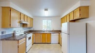 This single-floor residence features 2 bedrooms and 2 bathrooms within a practical and thoughtfully arranged floor plan. The U-shaped kitchen is outfitted with warm honey-toned wood cabinetry, dark laminate countertops, white appliances including a range, dishwasher, and refrigerator, and durable tile-style flooring. A window above the sink allows natural light to brighten the space. The adjoining living room is carpeted and features a sliding glass door that opens to an outdoor patio area, providing both natural light and exterior access. The primary bedroom offers a comfortable amount of space, complemented by a built-in closet with sliding wood doors, a small built-in countertop nook, and an en suite bathroom. The en suite includes a granite-style vanity countertop, a tub-shower combination, and tile flooring. The second bedroom is carpeted and simply designed, offering flexibility of use. The second full bathroom mirrors the finishes of the primary bath, featuring similar countertops, a tub-shower unit, and tile flooring. A hallway connects the bedrooms and bathrooms, adding to the overall flow of the layout. Neutral tones and textured ceilings are consistent throughout, creating a cohesive and clean aesthetic across the entire residence.