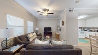 This two-floor residence carries a consistent coastal aesthetic throughout, with warm neutral tones and beach-inspired accents tying each space together. The living area on the main level is generously proportioned, featuring crown molding, a ceiling fan with integrated lighting, and multiple windows dressed with horizontal blinds that allow ample natural light. Comfortable seating arrangements surround a glass-topped coffee table, with a media console providing a functional focal point. The kitchen is fitted with white cabinetry, dark granite-style countertops, tile flooring, and white appliances, including a range, dishwasher, and built-in microwave. A staircase with wall sconce lighting connects the two levels. The bedrooms continue the coastal theme, with wave-patterned bedding, beach-themed artwork, and distressed wood headboards. One bedroom benefits from French doors, while another features elevated windows that draw in additional natural light. The bathroom is finished with tile flooring and a tub-shower combination. Throughout the residence, carpet flooring in the living and sleeping areas adds warmth, complementing the overall relaxed and inviting ambiance.