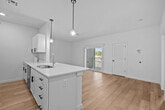 This well-appointed single-floor residence showcases a clean, modern design with thoughtfully selected finishes throughout. The heart of the home is an open-concept kitchen and living area, where light hardwood flooring flows seamlessly underfoot. The kitchen is equipped with white shaker-style cabinetry featuring matte black hardware, light countertops, and a full suite of stainless steel appliances including a range, over-the-range microwave, and refrigerator. A generous central island with an integrated sink serves as both a functional workspace and a natural gathering point, elegantly lit by two globe pendant lights suspended from above. Recessed lighting throughout the common areas ensures a consistently bright and welcoming atmosphere. The bedrooms offer plush wall-to-wall carpeting and crisp white walls, creating comfortable and restful retreats. Each bedroom benefits from natural light through well-placed windows with outdoor views. Closet space is well-considered, with one bedroom featuring double doors for ample storage. The bathroom is clean and functional, outfitted with a walk-in shower and light hardwood-style flooring that carries the home's consistent aesthetic. Overall, the space presents a fresh, move-in-ready environment with a cohesive neutral palette and contemporary detailing.