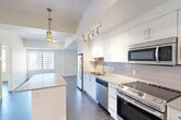 Located at 10045 111 St NW in Edmonton's vibrant Oliver neighbourhood, this well-designed one-bedroom, one-bathroom unit offers a thoughtful layout across a single floor. The kitchen is a standout feature, showcasing white cabinetry, quartz countertops, a subway tile backsplash, and a full suite of stainless steel appliances including a refrigerator, electric range, built-in microwave, and dishwasher. A central island with a quartz surface provides additional workspace and casual dining potential, while stylish pendant lighting adds a modern touch overhead. Dark hardwood-style flooring runs throughout the main living and kitchen areas, creating a warm contrast to the bright, white finishes. The bedroom offers a calm, neutral palette with light wood-tone flooring, and a large window frames views of the Edmonton skyline, allowing ample natural light. A dedicated closet provides practical storage. The bathroom is finished in a clean, contemporary style with a wide vanity, undermount sink, quartz countertop, white cabinetry, and a combined tub and shower enclosure with a curved rod. Neutral tile flooring ties the space together seamlessly. The overall ambiance is modern and functional, ideal for urban living.