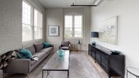 This single-floor, 2-bedroom, 2-bathroom residence showcases a compelling mix of industrial heritage and contemporary design. The living room is a standout space, characterized by soaring ceilings with white-painted wood planking, large arched and multi-pane windows that flood the room with natural light, and exposed painted brick walls that add textural depth. Wood-style flooring anchors the open layout, creating a warm, inviting atmosphere.

The kitchen is well-appointed with dark espresso cabinetry, stainless steel appliances including a refrigerator, range, microwave, and dishwasher, and light countertops that provide strong visual contrast. A large window brings additional natural light into the space.

Both bedrooms feature soaring ceilings with the same white-planked detail seen in the living area, plush carpeting, and generous windows. Each bedroom includes closet space, with one offering a walk-in closet fitted with wire shelving and hanging rods for organized storage.

The two bathrooms are finished with dark vanity cabinetry, white countertops, framed mirrors, and tub-shower combinations with decorative curtains. Light tile flooring ties each bathroom together with a clean, cohesive aesthetic throughout the residence.