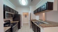 The Addington 2-bedroom, 2-bathroom unit is a single-story residence designed with a practical and comfortable layout. The galley-style kitchen is well-appointed with dark espresso cabinetry, granite countertops, a double stainless steel sink, and black stainless appliances including a range, microwave, and refrigerator. Light tile flooring and crown molding add a polished finish to the space, while a utility panel and access door lead to additional storage or laundry connections.

The living area is generously sized, featuring plush carpeting, crown molding, recessed lighting, and a ceiling fan. French doors open to the outdoors, filling the room with natural light and providing convenient exterior access. The open feel is further enhanced by neutral wall tones throughout.

Both bedrooms are carpeted and well-proportioned, each equipped with a ceiling fan and windows that invite natural light. The bedrooms offer easy access to their respective bathrooms, which feature wood-look flooring, dark vanity cabinetry with granite countertops, and a tub/shower combination. The overall aesthetic is cohesive and neutral, offering a clean and move-in ready environment.