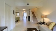 This two-story home offers a well-designed layout that balances openness with defined living spaces. The main level welcomes visitors with a bright, expansive entryway finished in large-format light tile flooring that extends throughout the common areas, creating a clean and cohesive aesthetic. A graceful arched passageway serves as a central architectural detail, framing the sightlines and adding a touch of classic elegance to the interior.

The entry opens naturally toward a formal dining area to one side, appointed with decorative furnishings and a warm, inviting ambiance. Straight ahead, a secondary arched opening leads to additional living space at the rear of the home, where natural light pours in through vertical blinds, brightening the entire main floor. A fireplace with a sleek dark surround adds a refined focal point to the living area.

A carpeted staircase with a clean white banister rises gracefully from the main level, providing access to the second floor. The staircase landing is neatly integrated into the open floor plan, maintaining the sense of spaciousness throughout. The overall ambiance of the home is bright, airy, and move-in ready, with neutral tones and architectural details that lend timeless appeal.