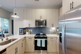 Located on Point Place in Mooresville, NC, this thoughtfully designed single-floor residence offers two bedrooms, two bathrooms, two closets, and a welcoming entrance that flows seamlessly through the home. The interior is defined by light wood-toned flooring, bold dark-painted panel doors with matte black hardware, and a cohesive modern aesthetic throughout.

The kitchen is a functional centerpiece, featuring light wood cabinetry extending to the ceiling, stainless steel appliances including a range and French door refrigerator, a crisp white countertop, and a striking blue subway tile backsplash accented by a pendant light fixture.

The primary bedroom is a vibrant retreat with rich green accent walls, natural light streaming through large windows with outdoor views, a ceiling fan, and ample space for furnishings. The second bedroom echoes a similarly refined design with soft gray tones, large windows overlooking the surrounding landscape, and a cozy window seating nook.

Each bathroom is well-appointed — one features a dual-sink vanity with white countertops and marble-tiled walls, while the other includes a single vanity with a glass-enclosed tub-shower combo and direct access to a dedicated closet. The living area rounds out the space with ceiling fans, bold accent walls, and natural light from oversized windows.