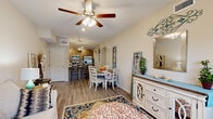 This well-appointed 2-bedroom, 3-bathroom single-story home in Clarksville, Tennessee offers a thoughtfully designed open-concept layout that maximizes both function and comfort. The combined living, dining, and kitchen area forms the heart of the home, with warm wood-look flooring flowing throughout. The living room features a ceiling fan with light fixture and a bright, welcoming atmosphere with natural light filtering through windows dressed with teal curtains. The kitchen is outfitted with light natural wood cabinetry, stainless steel appliances including a refrigerator, range, microwave, and dishwasher, along with clean white countertops that offer ample prep space. The dining area comfortably accommodates a full dining set and connects seamlessly to the living space. The spacious primary bedroom features plush carpeting, a tray ceiling detail, recessed lighting, and generous closet access. Its en-suite bathroom includes a double-sink vanity with wood cabinetry, white countertops, and a separate shower. The second bedroom is equally comfortable with soft carpeting. A second full bathroom features a tub-shower combination with glass sliding doors. Additional highlights include a laundry area, utility room, multiple closets, a hallway connecting the private quarters, and a patio for outdoor enjoyment.