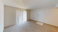 This single-floor residence offers a straightforward and functional layout across several well-defined spaces. The living area welcomes you through a white entry door and is bathed in natural light from large windows fitted with vertical blinds. Neutral-toned carpet runs throughout the living and bedroom areas, lending a cohesive and comfortable feel to the interior.

The bedroom is a spacious, quiet room with its own window, also dressed with vertical blinds, and features a closet with double doors alongside an additional door providing convenient access to adjacent spaces. The soft carpeting and cream-painted walls create a calm, restful atmosphere.

The kitchen stands out as the most distinctive room in the residence, boasting a striking full-height exposed brick accent wall that adds warmth and character to the space. Cream cabinetry lines the walls with ample upper and lower storage, complemented by a tile backsplash, a gas range, and a ceiling fan overhead. The flooring transitions to vinyl tile in this area, providing a practical surface for daily use.

The bathroom is clean and efficient, featuring a tiled tub-shower combination, a toilet, and a vanity with a granite-style countertop and wood cabinetry below. White tile flooring and bright walls keep the space feeling fresh and orderly. Throughout the unit, the design is simple and neutral, offering a versatile canvas ready for personalization.