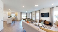 This two-story home is thoughtfully designed with a flowing open-concept layout on the main floor. The spacious living room serves as the heart of the home, featuring rich hardwood-style flooring, recessed lighting, and multiple windows dressed with neutral drapes that allow generous natural light. The living area transitions seamlessly into a dining space and a well-appointed kitchen outfitted with light wood cabinetry, white quartz countertops, stainless steel appliances, and hardwood-style flooring. A convenient half bath on the main level features a pedestal sink, oval mirror, and black hardware accents. A dedicated laundry room with full-size washer and dryer adds practical convenience.

Upstairs, the bedrooms are carpeted and bright, with windows offering outdoor views. Each bedroom provides a comfortable, well-proportioned retreat. A bonus sitting area or flex room offers additional living space with plush carpet. A full bathroom features a glass-enclosed walk-in shower with white subway tile surround and matte black hardware, reflecting a clean, modern aesthetic.

Throughout the home, a consistent palette of white walls, black hardware, and warm wood tones creates a cohesive and contemporary atmosphere.