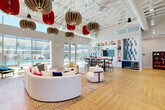 Located at 9910 W Montebello Ave in Phoenix, AZ, this single-story community clubhouse is a thoughtfully designed social hub that balances modern aesthetics with functional versatility. The space is anchored by soaring ceilings with an exposed structural grid, from which a striking collection of sculptural pendant lights in neutral tan and bold red tones cascade dramatically overhead, serving as a defining architectural focal point.

The main lounge area features warm herringbone-patterned hardwood flooring and is furnished with a curved white sectional sofa, accent chairs, and a patterned area rug, creating an inviting and stylish gathering zone. Floor-to-ceiling glass walls and sliding doors along one side flood the interior with abundant natural light while offering direct views of the outdoor pool and courtyard area.

A dining and bar zone includes a tall communal table with bar-height seating, positioned adjacent to a built-in feature wall of white open shelving accented by geometric blue tile, housing a large mounted television and a beverage refrigerator below.

A private conference or meeting room, enclosed by sliding frosted-glass and terracotta-toned panels, offers an intimate space with sage green walls, herringbone flooring, globe pendant lighting, and a white conference table with upholstered seating. The entryway features decorative etched-glass partitions and graphic wall art, setting a vibrant, contemporary tone upon arrival.