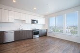 Located at 471 26th St in Oakland, CA, this modern single-floor unit offers a thoughtfully designed layout that maximizes every square foot. The open living area is bathed in natural light from large windows that frame views of the surrounding Oakland cityscape, complemented by warm wood-look flooring that flows throughout the space.

The kitchen is a standout feature, boasting a full suite of stainless steel appliances including a refrigerator, electric range, built-in microwave, and dishwasher. Two-toned cabinetry — combining white upper cabinets with wood-grain lower cabinets — lines the walls, offering generous storage alongside clean white countertops and a modern sink.

The hallway connects the living and kitchen areas to the bathroom and additional spaces, and conveniently houses an in-unit stacked washer and dryer behind louvered doors, along with a closet for added storage. The bathroom features large-format tile flooring, a glass-enclosed walk-in shower with tile surround, and chrome grab bars, reflecting both style and accessibility. The entrance welcomes residents with a clean, modern aesthetic consistent with the rest of the unit. Recessed lighting and a neutral white palette throughout create a bright, contemporary ambiance.