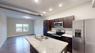 This thoughtfully designed 2-bedroom, 2-bathroom residence at 760 Main Street in Charlestown, Indiana offers a functional and modern living experience across a single floor. The open-concept layout seamlessly connects the kitchen, dining, and living areas, creating a spacious and inviting common space. The kitchen is a standout feature, equipped with rich dark-toned cabinetry, granite-style countertops, a central island with a double basin sink, and a full suite of stainless steel appliances including a range, over-the-range microwave, and side-by-side refrigerator. Exposed ductwork adds an industrial touch to the ceiling, complemented by recessed lighting throughout. Durable wood-style flooring extends across the main living areas, while the bedrooms feature plush carpeting and neutral warm-toned walls. Each bedroom receives natural light through windows with outdoor views. The two bathrooms are clean and functional — one featuring a walk-in shower with built-in shelving, the other a full tub-shower combination. Additional highlights include three closets for ample storage, a dedicated laundry area, and a hallway connecting the private spaces. This residence offers a comfortable, practical layout well-suited for everyday living.