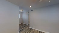 This 1-bedroom, 1-bathroom unit is thoughtfully laid out across a single floor, offering a compact yet functional living environment. The interior features wood-look vinyl plank flooring in a warm gray-brown tone, providing a modern and durable foundation throughout the space. Neutral light gray walls create a clean, versatile backdrop that complements a variety of décor styles. Recessed lighting and flush-mount ceiling fixtures provide consistent illumination, while HVAC vents integrated into the ceiling and walls ensure year-round climate comfort. White baseboards add a crisp, finished look to each room. Natural light filters in through a window in the bedroom area, brightening the space and contributing to an open, airy feel. The layout includes a dedicated bedroom with access to a closet area, as well as a bathroom. The overall design is clean and contemporary, with attention to practical details that make everyday living comfortable. This unit is well-suited for individuals or couples seeking a straightforward, low-maintenance living space with modern interior finishes.