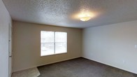 This single-floor residential space offers a straightforward and functional layout designed for comfortable everyday living. The interior is characterized by its textured popcorn ceilings, which add a classic finish throughout the space, complemented by neutral-toned walls that create a warm and inviting atmosphere.

The carpeted flooring runs throughout the space, providing a soft and comfortable underfoot experience. Each room is equipped with ceiling-mounted flush light fixtures that ensure consistent illumination across the interior. Windows fitted with horizontal blinds allow natural light to filter in while maintaining privacy, and offer views of the surrounding exterior.

The rooms feature clean wall lines with white baseboards that provide a neat contrast against the neutral wall color. The overall design is simple and practical, prioritizing livability and ease of use. The single-floor layout ensures convenient accessibility throughout, with no stairs or level changes to navigate. The space presents a blank canvas well-suited for personalization, making it an adaptable environment for a variety of living arrangements.