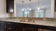 Located at 4600 Spotsylvania Pkwy in Fredericksburg, Virginia, this single-floor residence offers a thoughtfully designed layout with a range of quality finishes and generous living spaces. The open-concept kitchen serves as a functional centerpiece, showcasing dark espresso cabinetry, granite countertops with a complementary tile backsplash, and stainless steel appliances including a range, microwave, and dishwasher. A large undermount sink anchors the kitchen island, which is illuminated by a trio of pendant lights. The kitchen opens directly to the living area, which features crown molding, a ceiling fan, and French doors with transom windows that invite abundant natural light and outdoor views.

The bedrooms are carpeted and generously proportioned, each benefiting from multiple windows with wooded views and ceiling fans for comfort. One bedroom includes direct access to a walk-in closet outfitted with multi-tier wire shelving, providing considerable storage capacity. The bathroom features wood-look vinyl plank flooring, a dark vanity with granite countertop, a natural light window, and clean, neutral finishes. Throughout the residence, neutral tones, crown molding in key areas, and consistent material choices create a cohesive and comfortable living environment.