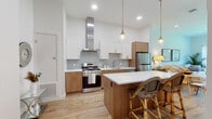 Located at 50 Peter Kristof Way in Medfield, Massachusetts, this thoughtfully designed single-floor residence combines modern finishes with a warm, inviting atmosphere. Light-toned hardwood flooring flows throughout the open layout, creating a seamless sense of continuity between living areas.

The kitchen is a standout feature, showcasing a two-tone cabinetry design with crisp white upper cabinets and natural wood lower cabinets, all accented by brushed gold hardware. A stainless steel gas range sits beneath a sleek wall-mounted range hood, complemented by a soft gray subway tile backsplash and white quartz countertops. A center island with bar seating and pendant lighting overhead makes the space ideal for both cooking and casual dining.

The living room is bright and airy, benefiting from large windows that frame views of the surrounding greenery and allow generous natural light to fill the space. Vaulted ceiling lines enhance the open feel of the room.

The bedrooms are tranquil retreats, with one featuring a window overlooking the outdoors, adding to the serene atmosphere. The bathroom is finished to a high standard, featuring a marble-surround walk-in glass shower, a wood-toned vanity with white countertop, and clean, neutral tiling throughout. The overall design is cohesive, modern, and move-in ready.